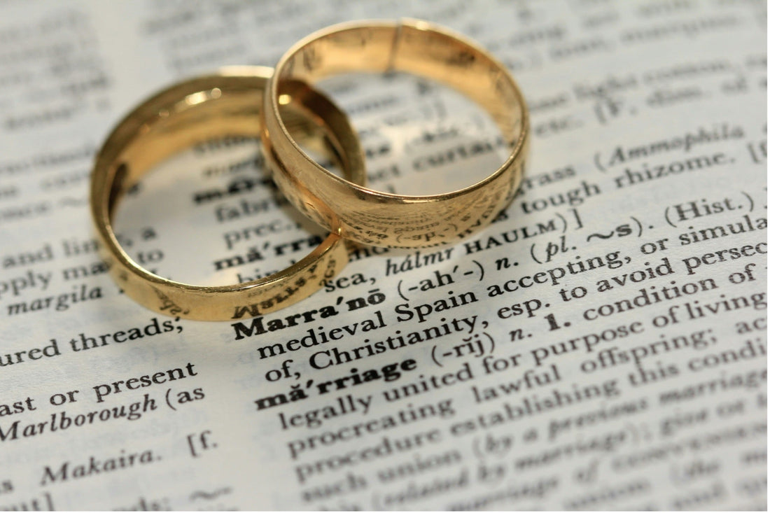 Gold men's wedding rings displayed on a dictionary definition of marriage